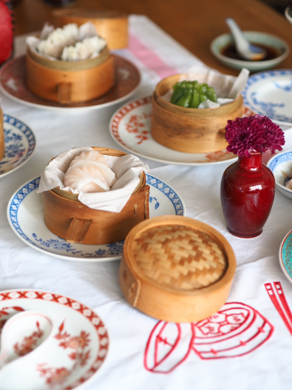 Dumplings in wooden steamers on with a white tablecloth, with a red dim sum basket and baguette embroidery