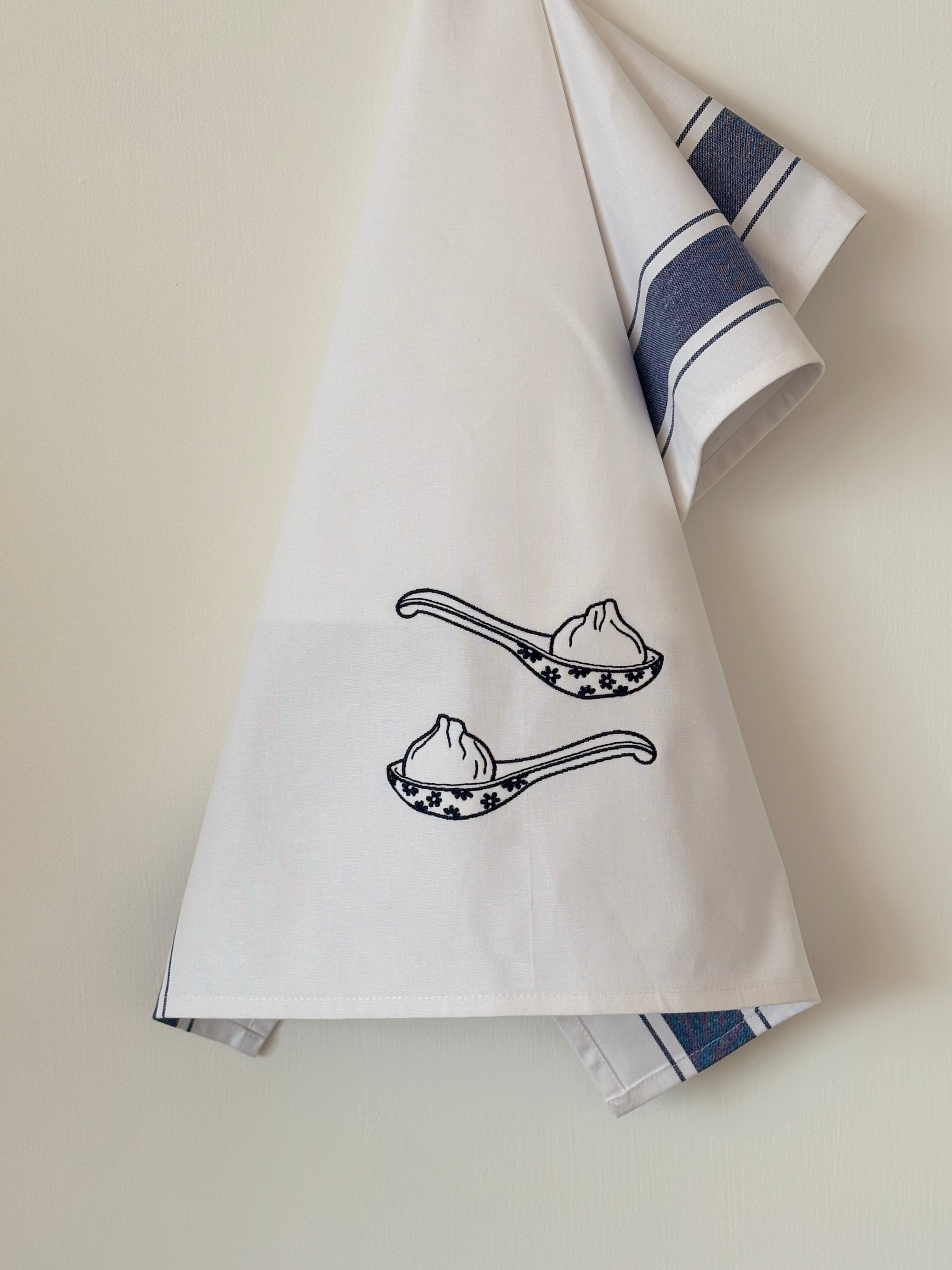 White towel with black illustrations of spoons and dumplings on a beige background