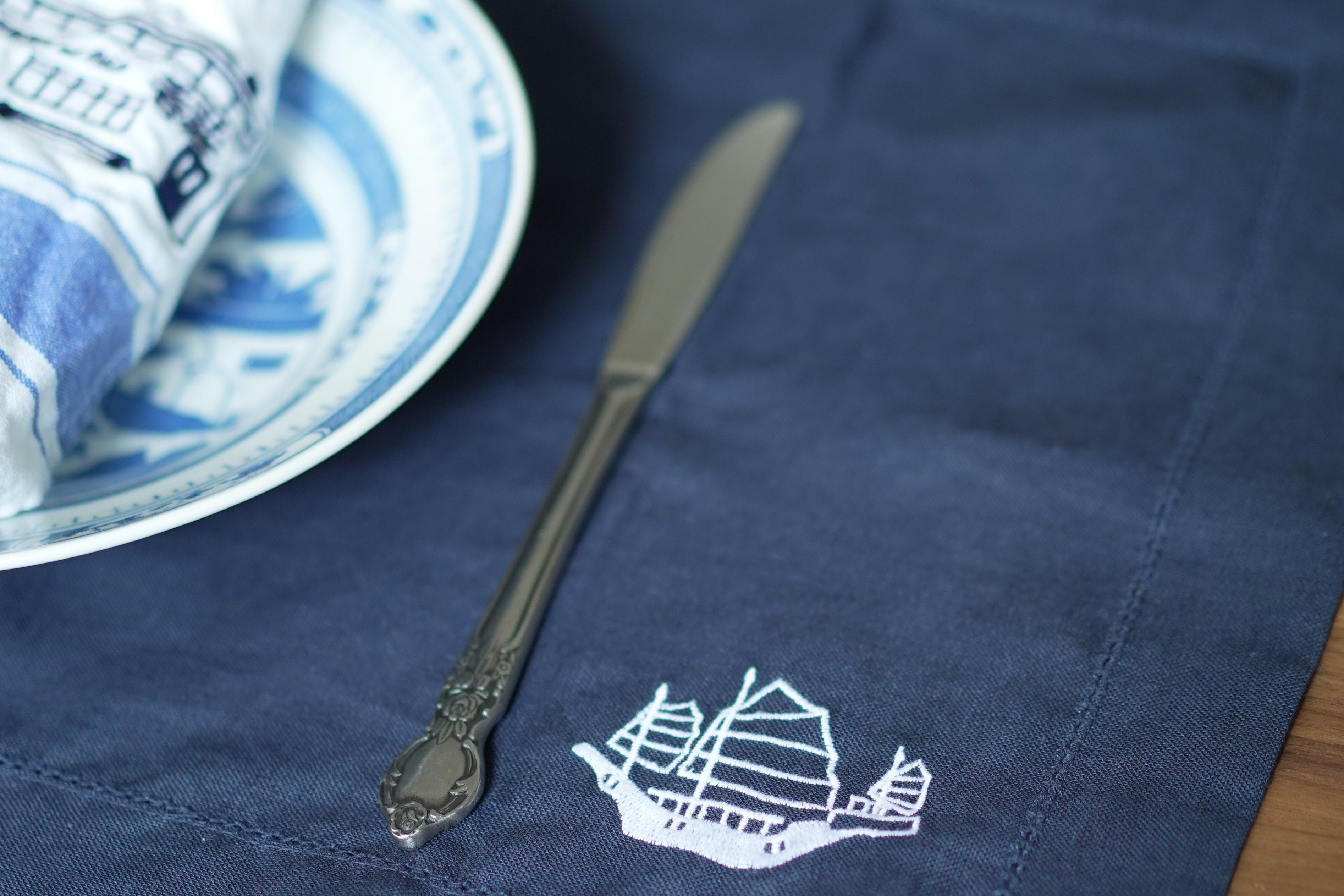 Navy blue placemat with a junk design embroidered on it, with plate and  napkin with hong-kong design.